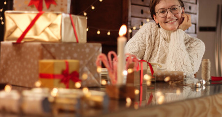 Woman in thick white cable sweater wrapping presents on the background of Christmas decorations and lights
