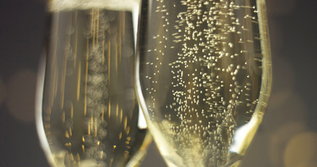 Bottle of sparkling wine with three flute glasses with bubbles floating up on gray backgrounds with Christmas lights