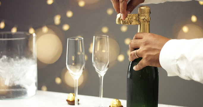 Close up slowmotion of man's hands opening a bottle of champagne on gray background with lights and flares