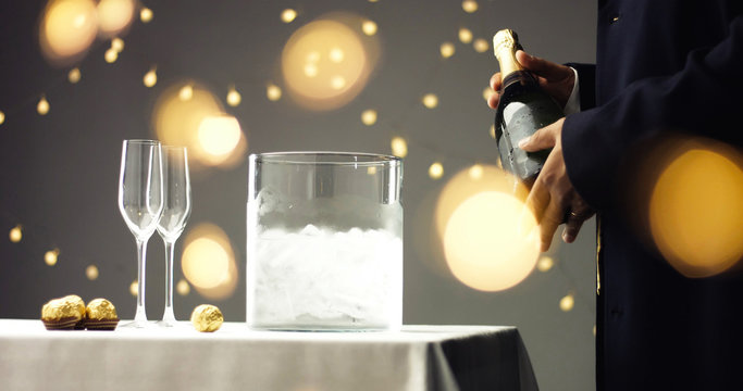 Close up video of taking a chilled bottle of sparkling wine out of a clear glass ice bucket on white, gray and golden background