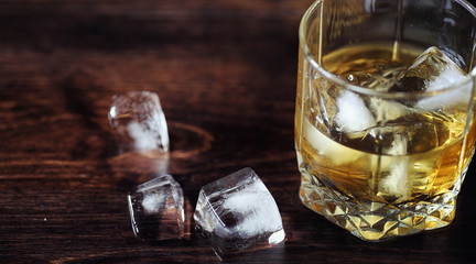Whiskey with ice with a glass. Cubes of ice on a wooden table an
