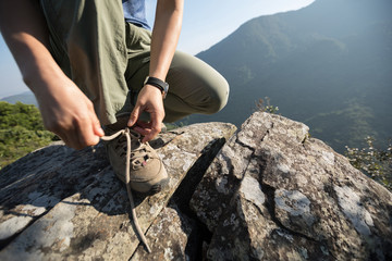 successful woman hiker tying shoelace on mountain top cliff edge