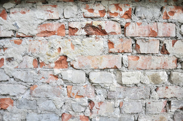 rough red brick wall after the removal of the facade , with the remnants of cement and plaster