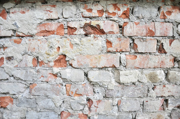 rough red brick wall after the removal of the facade , with the remnants of cement and plaster