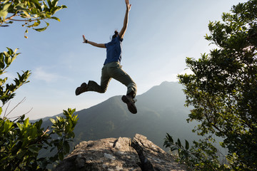 young woman jumping on cliff's edge with raised hands to the sunrise