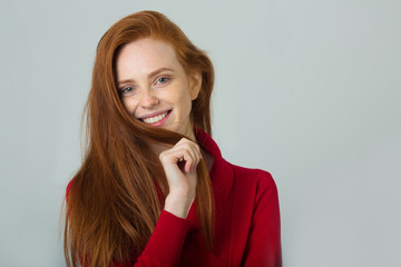 beautiful young smiling girl with red hair in a red sweater on a light background