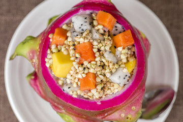 Fresh tropical fruit salad with green buckwheat and honey in dragon fruit skin, close up
