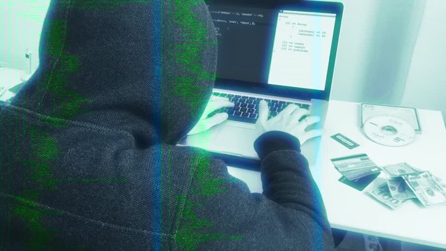Hooded Hacker Attacks In Cyberspace, Dolly Shot. Hooded person typing in a laptop next to stolen itens, simulating a hacker crime scene