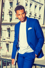 African American Businessman working in New York. Wearing blue suit, white T shirt, carrying laptop computer, black college student, standing by vintage building on campus, looking down, thinking..