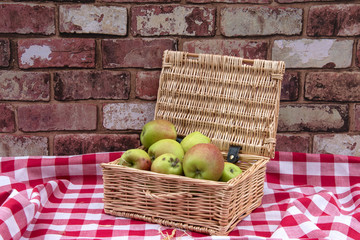 Wicker basket of apples on a red and white gingham tablecloth.