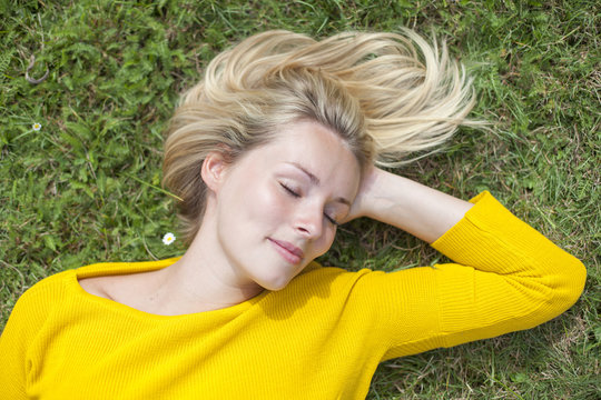 Portrait of a pretty blond woman lying down in the park with closed eyes
