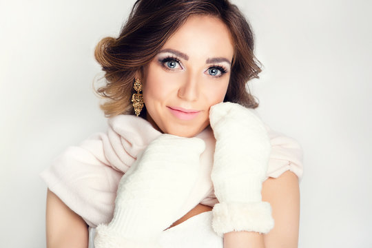 Model in a winter image on a white background. Beautiful girl with styling and makeup in mittens and a scarf