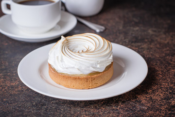 Delicious Lemon tart tartlet with meringue and cup of hot coffee on dark stone concrete table background. Copy space