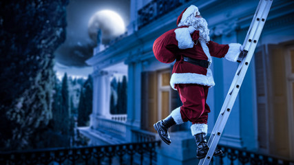 Santa Claus straddles the ladder. The magical vigiline night. The sky is full of stars and the big moon. - obrazy, fototapety, plakaty