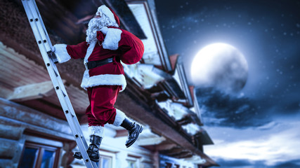 Santa Claus straddles the ladder. The magical vigiline night. The sky is full of stars and the big moon.
