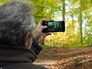 Älterer Mann im Herbstwald fotografiert mit seinem Smartphone