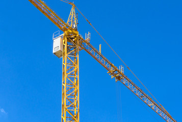 Yellow construction tower crane against blue sky