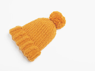 Fototapeta na wymiar Mustard knit beanie hat with big pom pom isolated on white background. Copy space. Flat lay. Top view