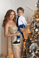 Happy mother and baby sitting near the luxury decorated Christmas tree in white and gold colors. New Year's holidays with family.
