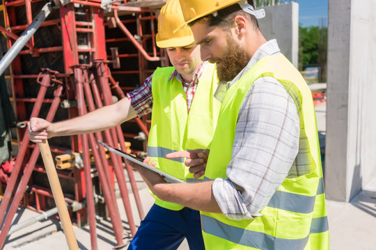 Two young construction workers smiling while using a tablet during break at work