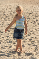 Charming blond girl walking along sandy beach