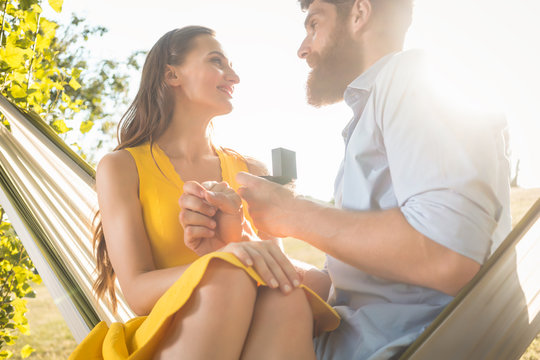 Young man making marriage proposal to beautiful girlfriend while swinging in hammock