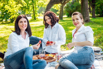 Young beautiful girls eating strawberries in the park