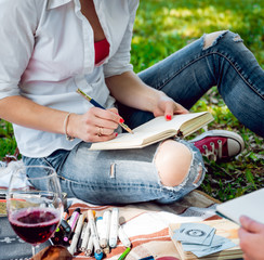 Young beautiful girls drawing the pictures in sketchbook. At the park