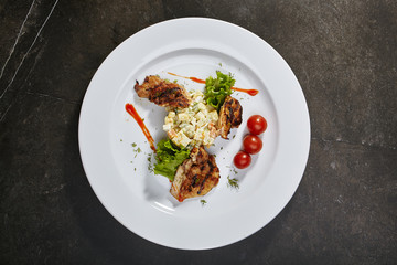 Olivier salad with grilled chicken, fresh herbs and cherry tomatoes on black background