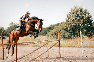 Young female jockey on horse leaping over hurdle