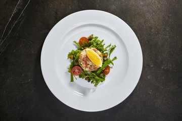 Salad Olivier with salmon with an orange slice and fresh herbs on black background