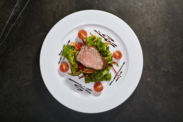 Roast beef with mixed salad and cherry tomatoes on black background