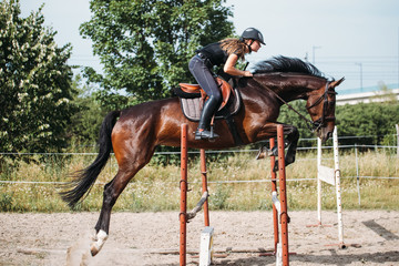 Obraz premium Young female jockey on horse leaping over hurdle