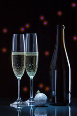 Два бокала шампанского,бутылка и новогодний шар на чёрном фоне