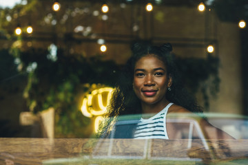 Teenager hipster ecuadorian woman viewed through window cafeteria and looking at camera. Relaxing,...