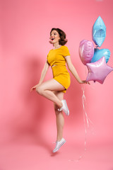 Cheerful young woman in yellow dress holding ballons