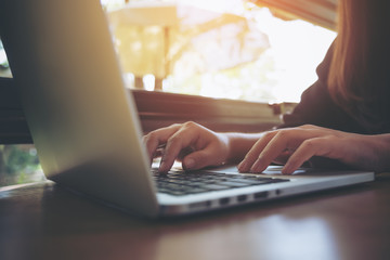 Closeup image of a business woman's hands working and typing on laptop keyboard on wooden table