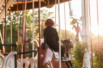 Cild on a carousel at a carnival or festival at sunset. Decorative ornate camel, animals at an...