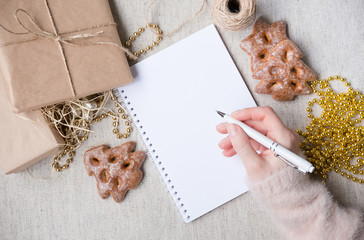 Christmas presents next to gold beads, gingerbread and cones hand writing in a notebook