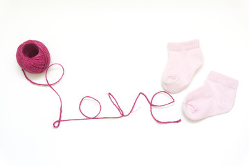 Word love written with pink wool thread and baby stockings on white background