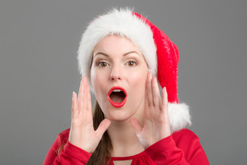Junge Frau mit Weihnachtsmütze hält Hand an den Mund und ruft