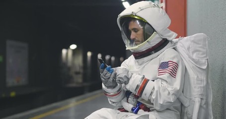 An astronaut dressed man uses the smartphone to call and send messages. The astronaut smiles while looking at the phone in his hand. Concept of: Phone Promotions, Messages and Spatial Calls. - Powered by Adobe