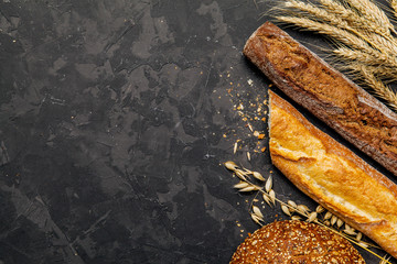 Top view of rustic bread, french baguette and wheat on dark background . Rural kitchen or bakery -...