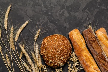 Tuinposter Top view of rustic bread, french baguette and wheat on dark background . Rural kitchen or bakery - background with free text space.  © chedima