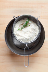flour in a sieve in a large metal bowl on a wooden table