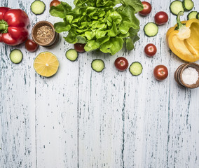 Ingredients for cooking vegetarian salad, bell peppers, cucumbers, cherry tomatoes, lettuce leaves, salt and black pepper, lime lined on a white rustic background, top view, close up, border, 