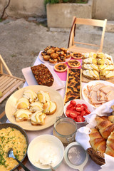 Table with various brunch food: goat cheese and pear sandwiches, ham, croissants, scrambled eggs, mushroom tart, blueberry muffins, banana bread, cream cheese and hazelnut spread. Top view. 
