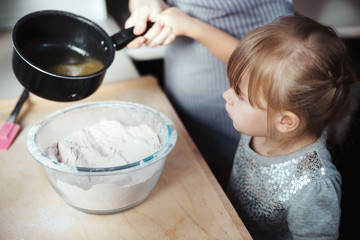 Young girl mixing ingredients for baking, pouring liquid into a bowl with flour. Lifestyle image at home kitchen, copy space.