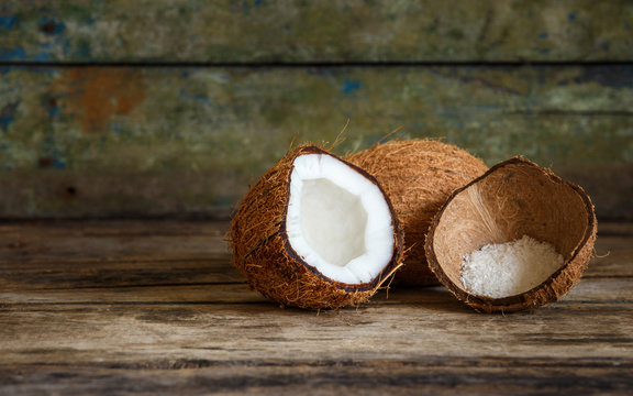 Fresh whole and cut in half coconuts with coconut flakes in shell on wooden background with copy space