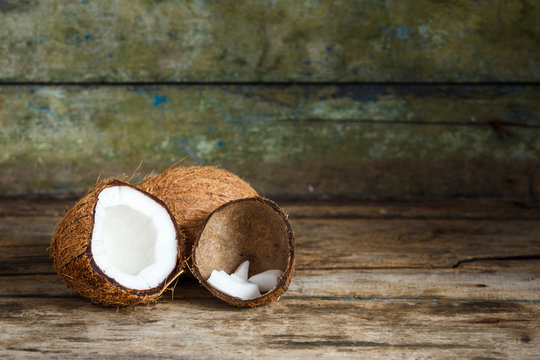Fresh whole and cut in half coconuts with coconut shreds in shell on wooden background with copy space